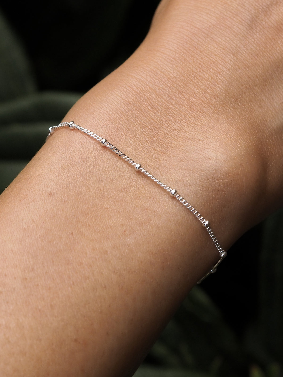 Close-up of a model wearing a minimal sterling silver satellite chain bracelet, highlighting its sleek and modern design.