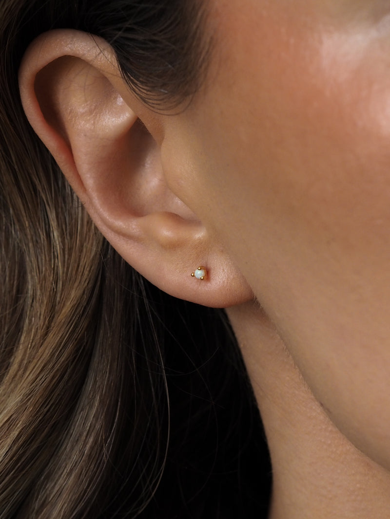 Close up of a model wearing delicate gold opal stud earrings.