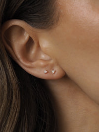 A model wearing two delicate sterling silver white opal stud earrings, layered together on one ear.