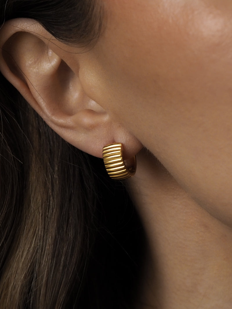 A close-up of a woman's ear wearing a chunky ridged gold hoop earring from Aluna Mae.