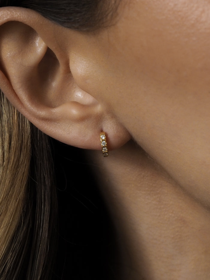 Close-up of a woman's ear wearing an 18ct gold-plated huggie earring with channel-set cubic zirconia stones.