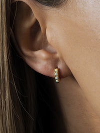 Close-up of a woman's ear wearing a small gold opal huggie earring by Aluna Mae
