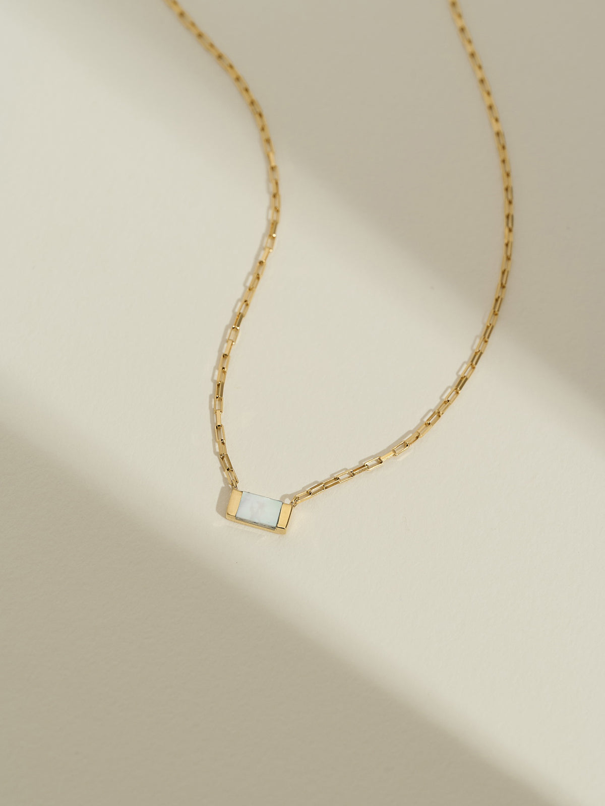 Close-up of a gold box chain necklace with a mother of pearl gemstone.