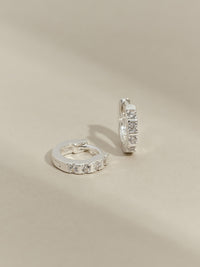 Close-up of sterling silver cubic zirconia huggies against a plain backdrop.