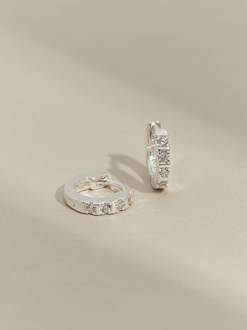 Close-up of sterling silver cubic zirconia huggies against a plain backdrop.