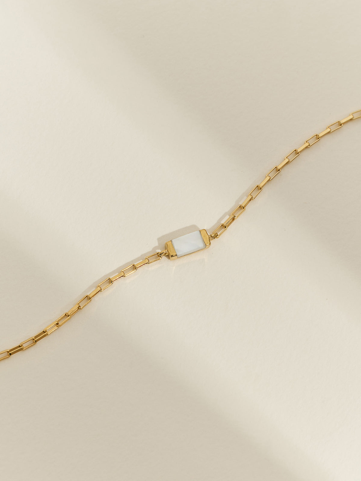 Close-up of a gold box chain bracelet with a mother of pearl gemstone.