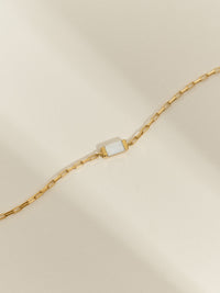 Close-up of a gold box chain bracelet with a mother of pearl gemstone.