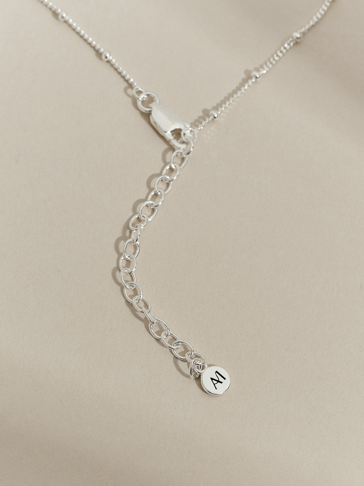 Close-up of a sterling silver satellite chain necklace with extender chain and Aluna Mae logo tag.