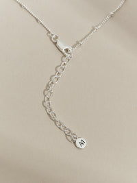 Close-up of a sterling silver satellite chain necklace with extender chain and Aluna Mae logo tag.