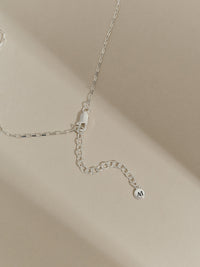 Close-up of a sterling silver box chain necklace with extender chain and Aluna Mae logo tag.