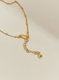 Close-up of a gold satellite chain bracelet with extender chain and Aluna Mae logo tag.