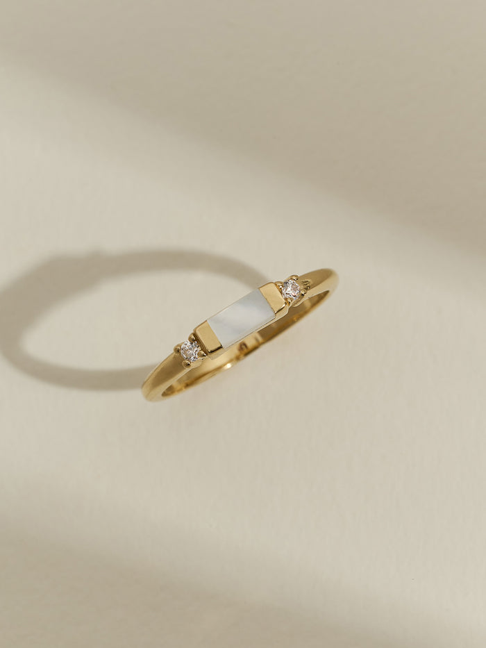 Close-up of gold vermeil mother-of-pearl and cubic zirconia ring against a plain backdrop.