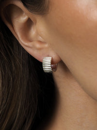 Sterling silver ribbed hoop earring worn on ear, shown in close-up.