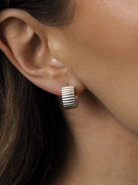Close-up of a sterling silver ribbed hoop earring worn on a model's ear.