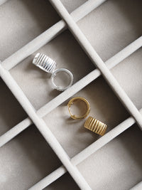Gold and silver ribbed hoop earrings displayed in a beige velvet jewellery organiser.