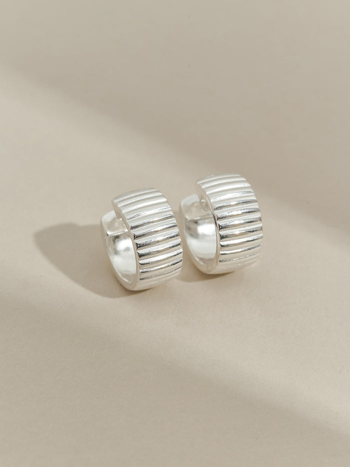 Pair of sterling silver ribbed hoop earrings displayed on a neutral beige background.
