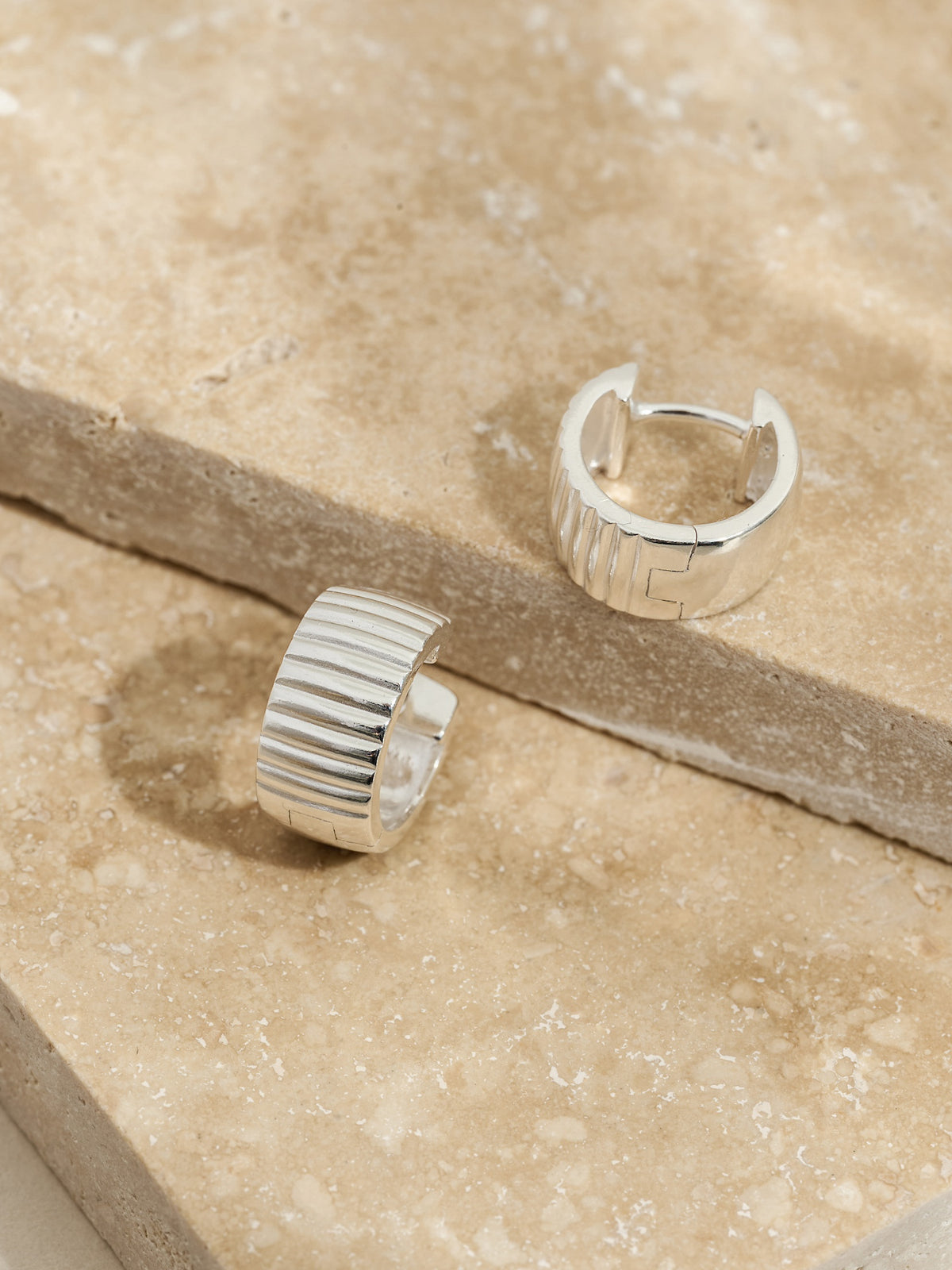 Sterling silver ribbed hoop earrings styled on stacked travertine stone slabs.