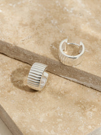 Sterling silver ribbed hoop earrings styled on stacked travertine stone slabs.