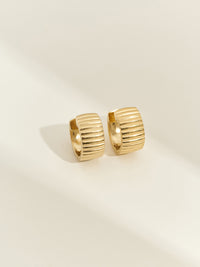 Close-up of ridged gold chunky hoop earrings from Aluna Mae, photographed on a cream background with soft natural lighting.