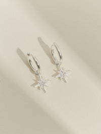 Sterling silver star hoop earrings displayed on a neutral background, featuring a polished hoop and eight-pointed star pendants with pavé detailing.