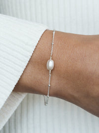 Delicate freshwater pearl bracelet with a sterling silver satellite chain, worn on a wrist with a white textured sleeve—perfect for bridesmaids or bridal gifting