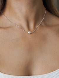 Freshwater pearl necklace with a sterling silver satellite chain, worn on a model with a white ribbed top.