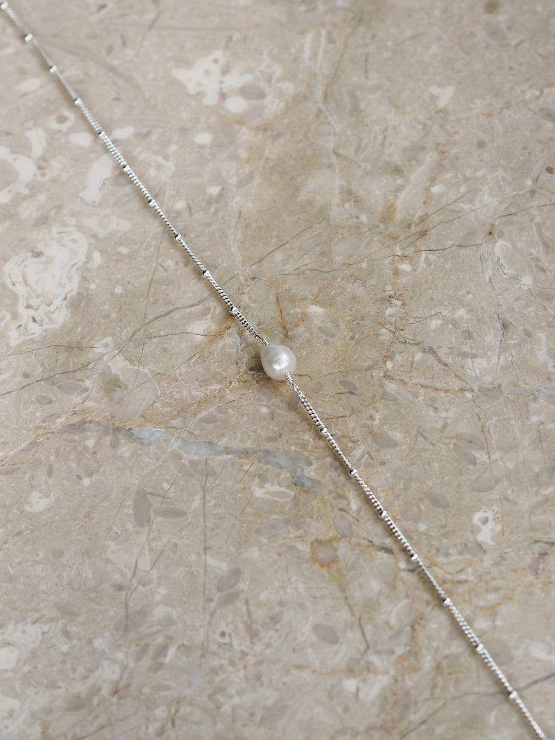 Freshwater pearl necklace with a sterling silver satellite chain, displayed on a neutral marble surface.