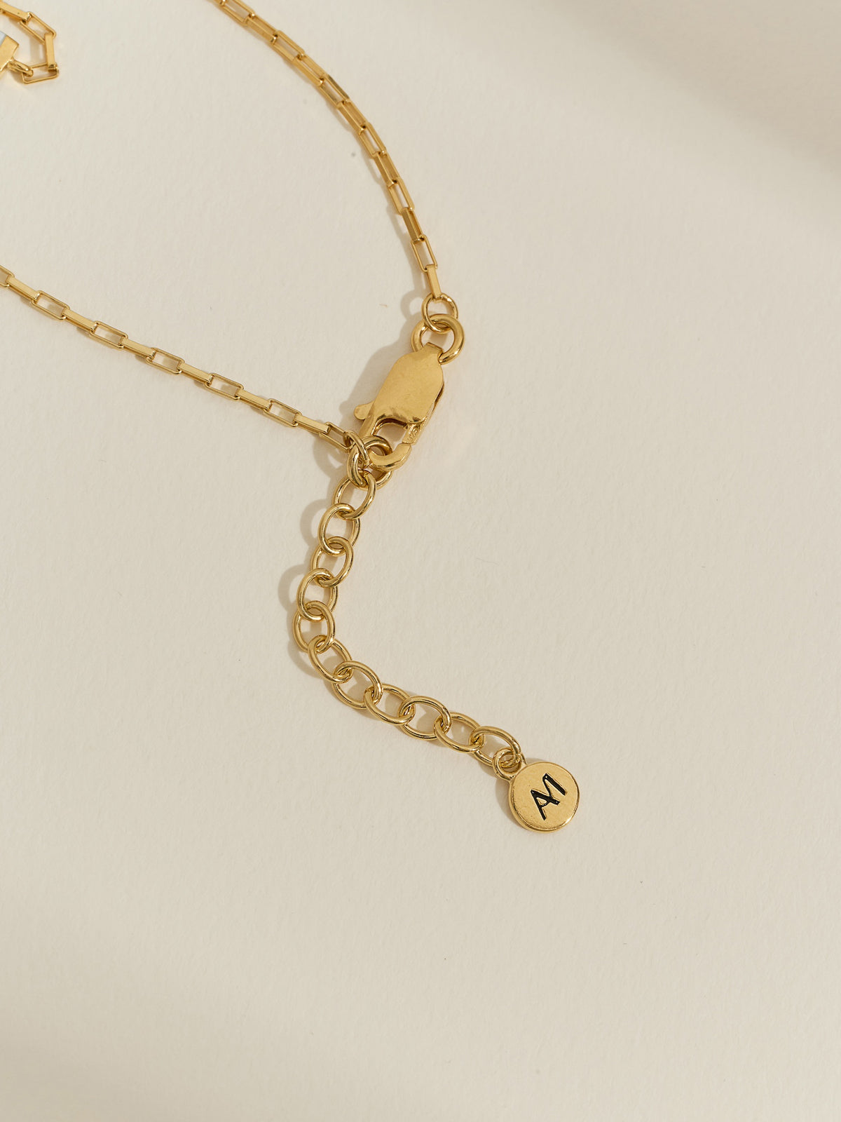 Close-up of the extender chain and lobster clasp on an 18ct gold-plated box chain bracelet, finished with an engraved Aluna Mae tag.