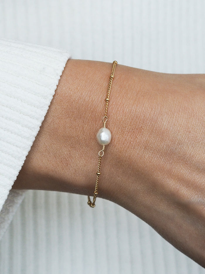 Gold freshwater pearl bridesmaid bracelet with satellite chain, worn on a wrist with a white ribbed sleeve.