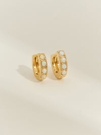 Pair of gold-plated huggie earrings set with five iridescent opal stones, photographed against a soft cream background.