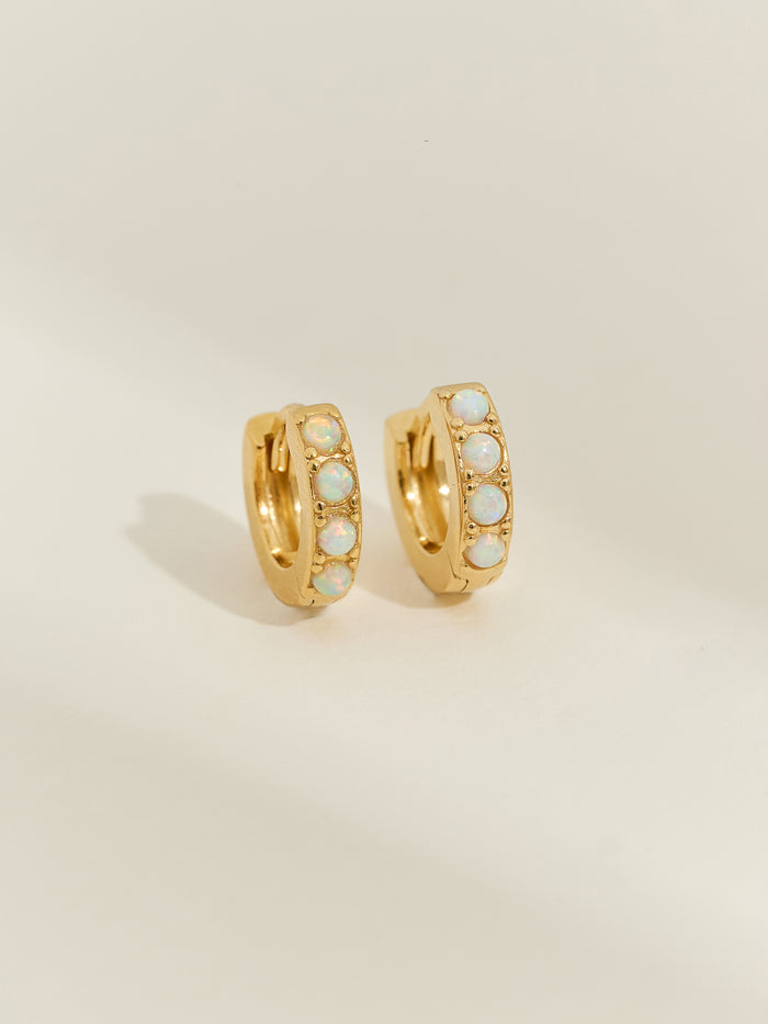 Pair of gold-plated huggie earrings set with five iridescent opal stones, photographed against a soft cream background.