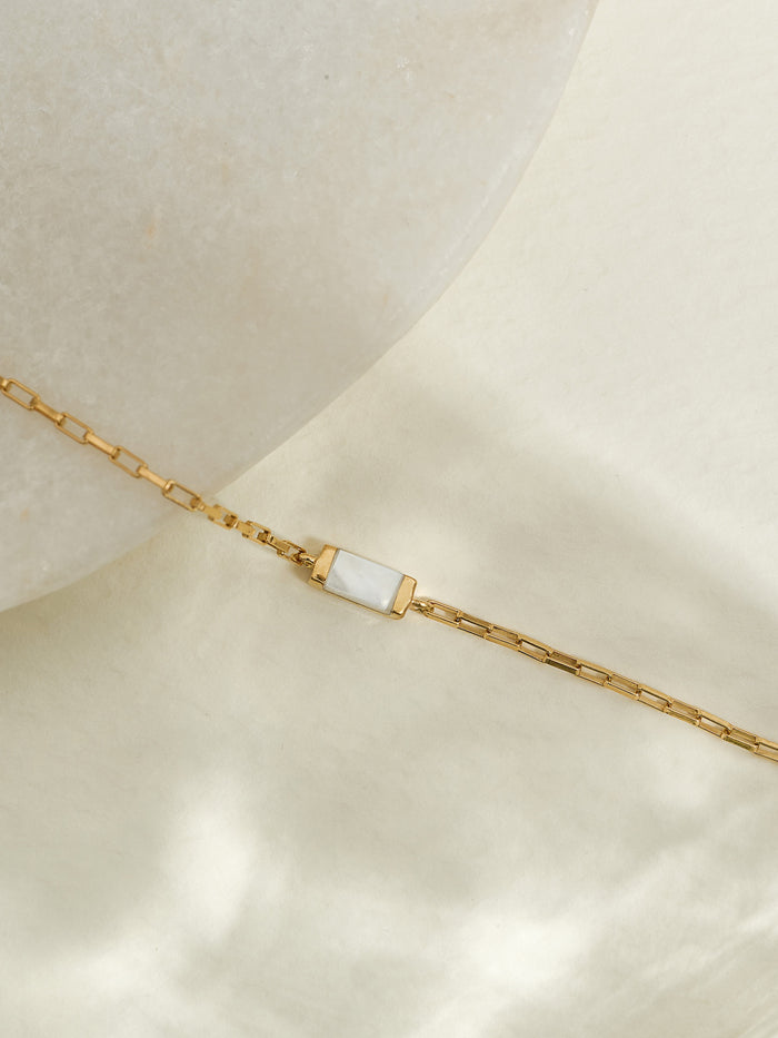 Close-up of a June birthstone bracelet featuring a rectangular mother of pearl stone set on a radiant 18ct gold plated box chain, displayed on a soft cream background with a smooth stone.