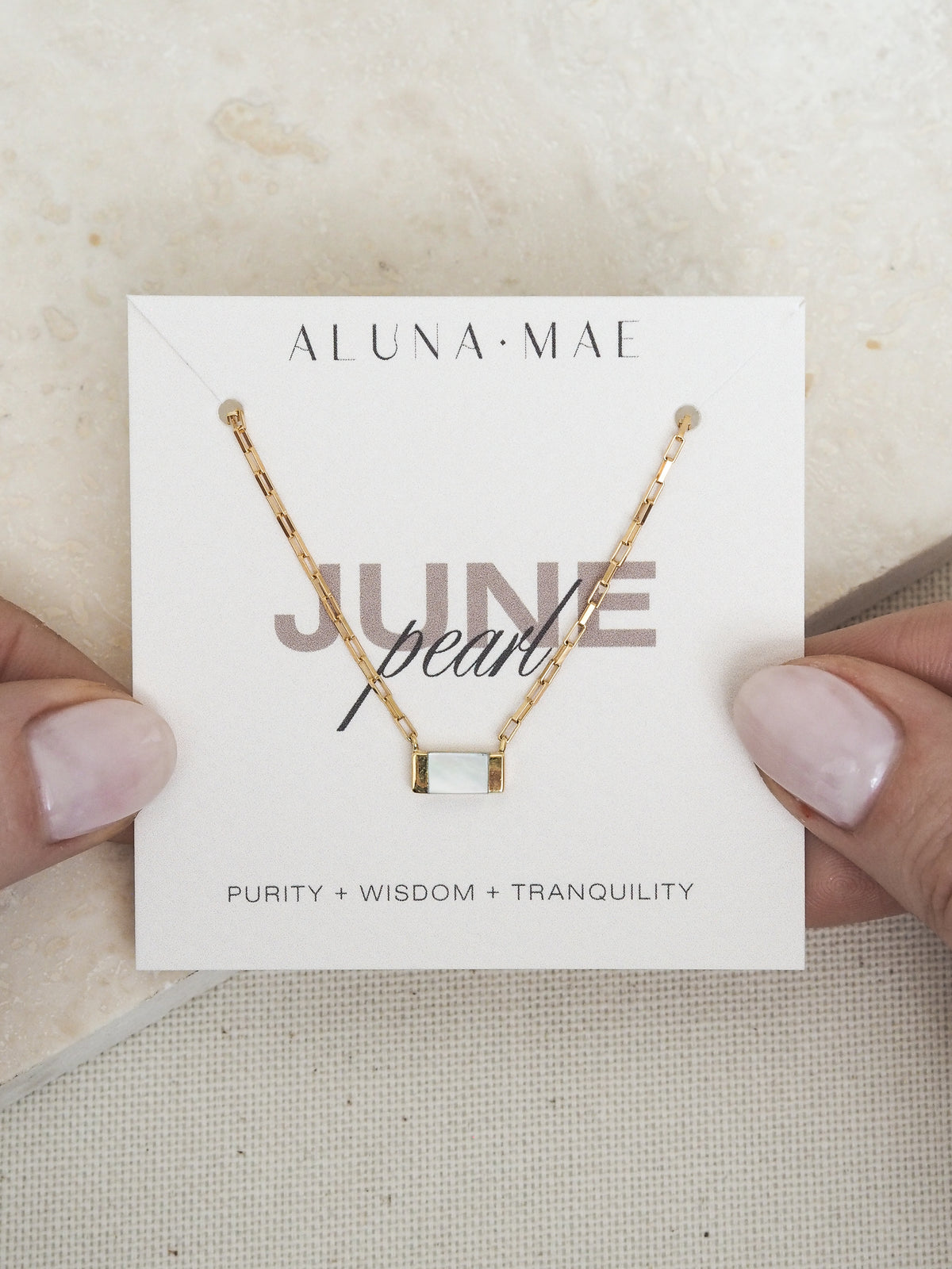 June birthstone necklace by Aluna Mae, featuring a rectangular mother of pearl pendant on a gold box chain, displayed on a card with gemstone meaning.