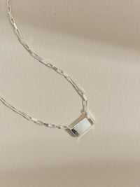 Close-up of a sterling silver necklace with a rectangular mother of pearl pendant on a box chain, styled on a neutral background.
