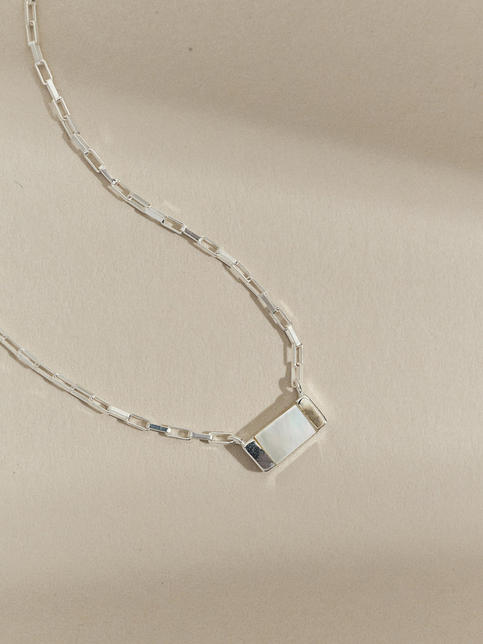 Close-up of a sterling silver necklace with a rectangular mother of pearl pendant on a box chain, styled on a neutral background.