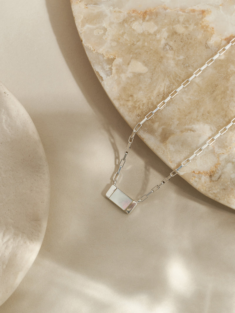 Sterling silver necklace featuring a rectangular mother of pearl pendant on a box chain, styled on a travertine stone surface with soft natural light.