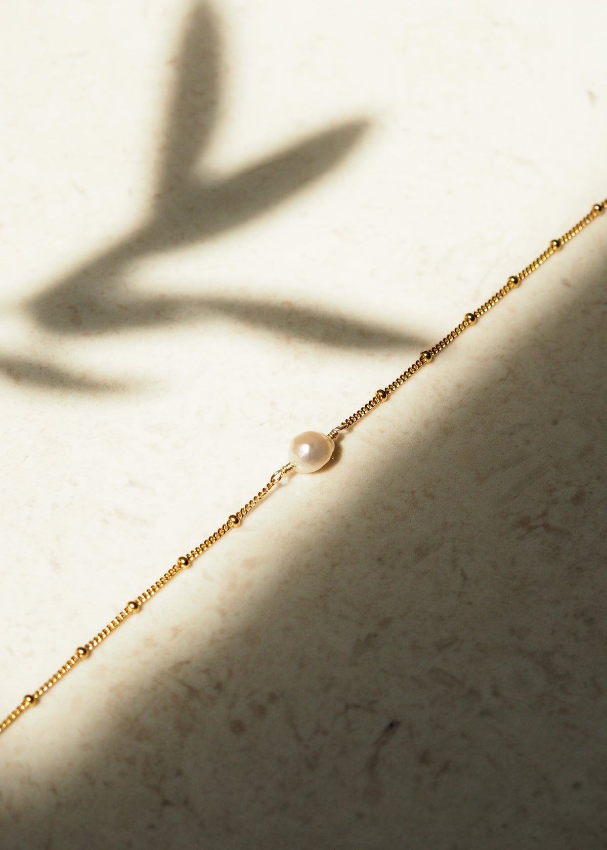 Close-up of a single freshwater pearl set on a delicate 18ct gold plated sterling silver satellite chain, photographed in natural light with soft shadows.
