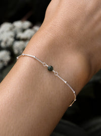 Close-up of a model's wrist wearing a May birthstone bracelet with a green emerald gemstone, on a delicate sterling silver chain.