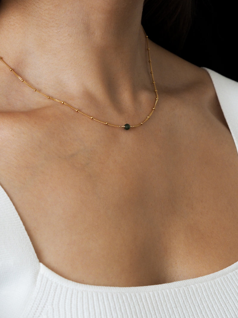 Close-up of a model wearing a May birthstone necklace with a green emerald gemstone, set on a delicate 18ct gold-plated sterling silver chain.