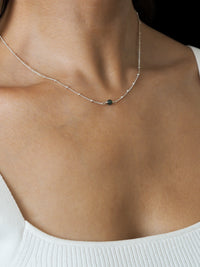 Close-up of a model wearing a May birthstone necklace with a green emerald gemstone, on a delicate sterling silver satellite chain.