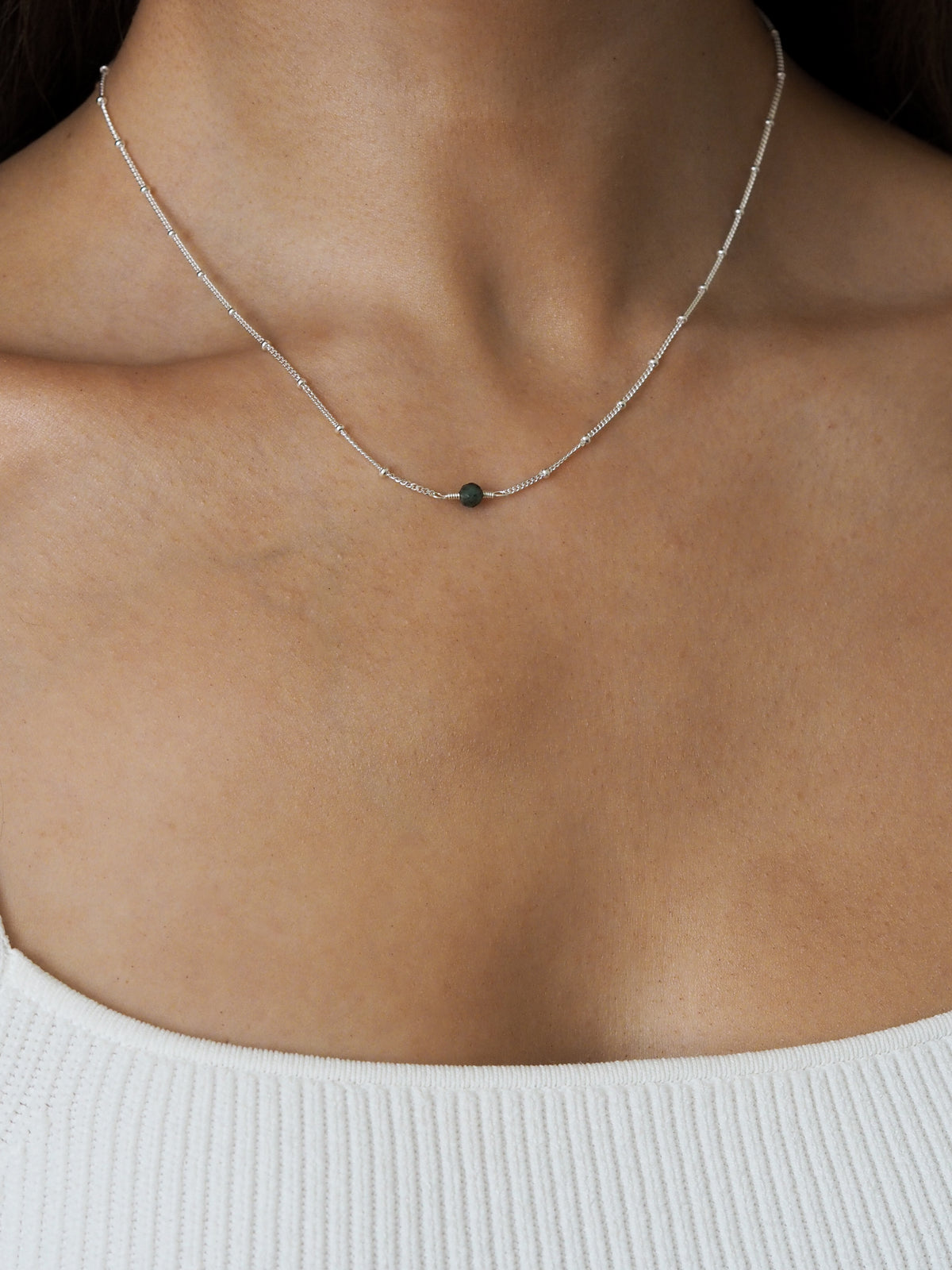 Close-up of a model wearing a May birthstone necklace with a green emerald gemstone, set on a delicate sterling silver satellite chain.