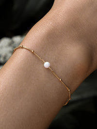 Close-up of a model's wrist wearing an October birthstone bracelet with a white opal gemstone, on a delicate 18ct gold-plated sterling silver chain.