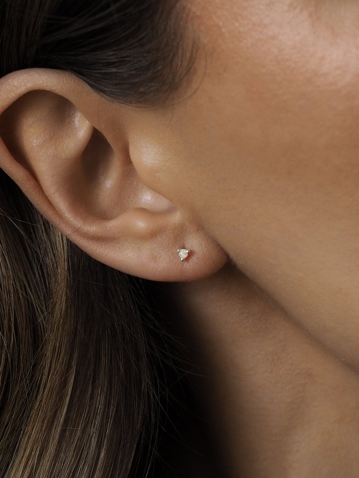 Close-up of a model wearing a pair of October birthstone opal gemstone stud earrings, set in sterling silver, on the ear.