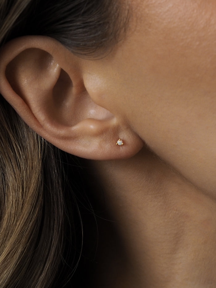 Close-up of a model's ear wearing an October birthstone opal gemstone stud earring, set in 18ct gold-plated sterling silver.