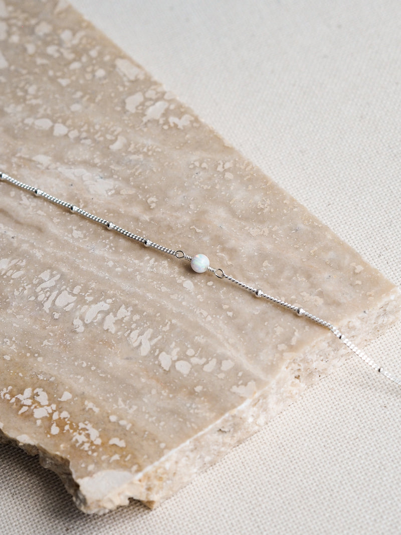 Close-up of October opal birthstone necklace with sterling silver satellite chain on stone background
