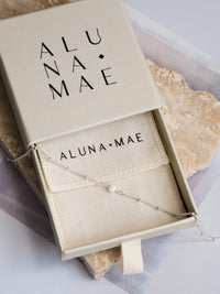 Aluna Mae necklace with a white opal gemstone on a sterling silver satellite chain, displayed in a gift box with the brand name visible.