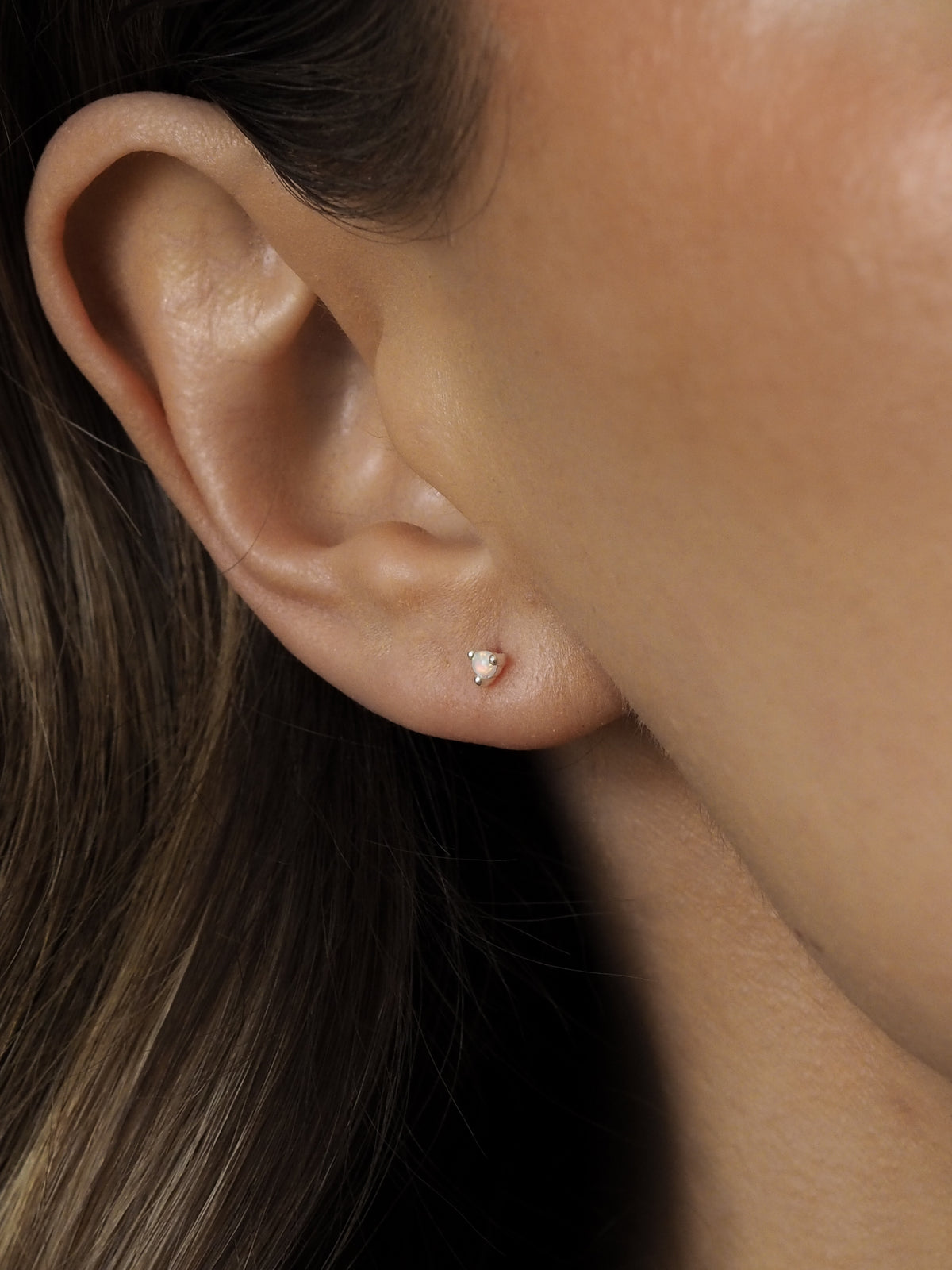 Close-up of a model's ear wearing an October birthstone opal gemstone stud earring set in sterling silver.
