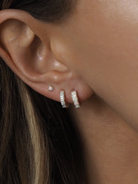 Close-up of a woman's ear wearing a trio of sterling silver earrings: a small opal stud, a cubic zirconia huggie, and a huggie set with round opal stones.