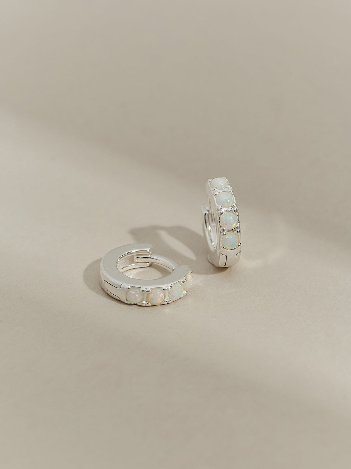 A pair of sterling silver huggie hoop earrings set with five round opal stones, displayed on a neutral-toned background.