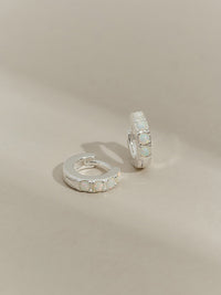 A pair of sterling silver huggie hoop earrings set with five round opal stones, displayed on a neutral-toned background.